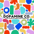 A colorful abstract patterned graphic with the text 'the DOPAMINE CO. YOUR FAVORITE MOBILE BAG CHARM BAR' in the center.